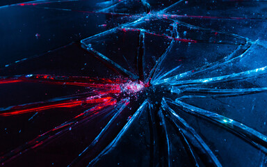 Close-up photo texture of blue and red toned broken and cracked glass on black backdrop.