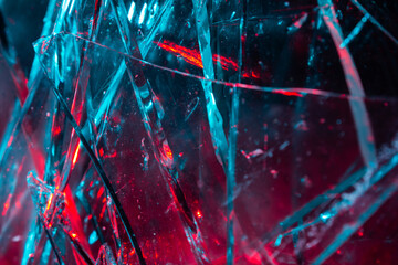 Close-up photo texture of blue and red toned broken and cracked glass on black backdrop.