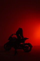 Fototapeta na wymiar teen leisure. silhouette young brunette girl sits fashion on a sports motorcycle on dark background in red light. lifestyle fashion concept, free space