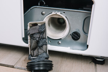 Male hand removes dirty and clogged washing machine pump filter. Services for the repair of...