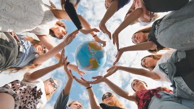 Earth conservation concept. 11 girls surround the rotating earth globe with their palms.