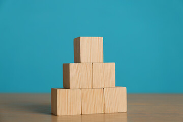 Pyramid of blank cubes on wooden table against light blue background. Space for text