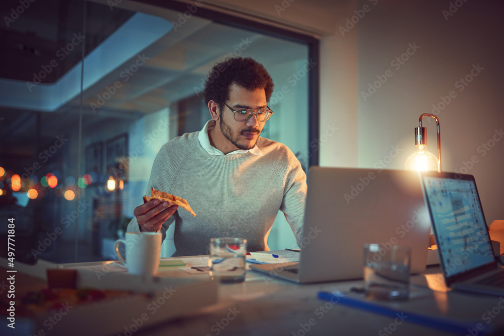 Poster getting some energy for another late night. shot of a young designer eating pizza while working late