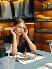 an attractive young girl sits at a table in a boudoir.