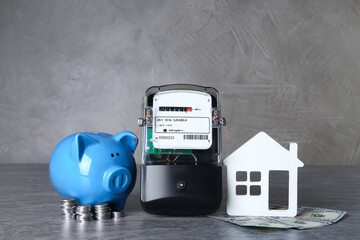 Electricity meter, piggy bank, house model and dollar banknotes on grey table
