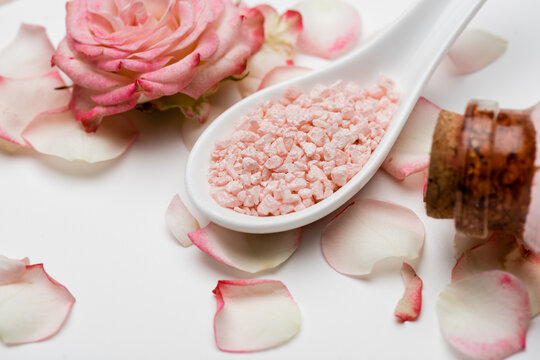close up view of flower near petals and pink sea salt on white.