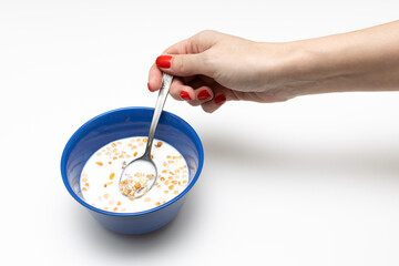 female hand holds a spoon with cereal over a cup with milk
