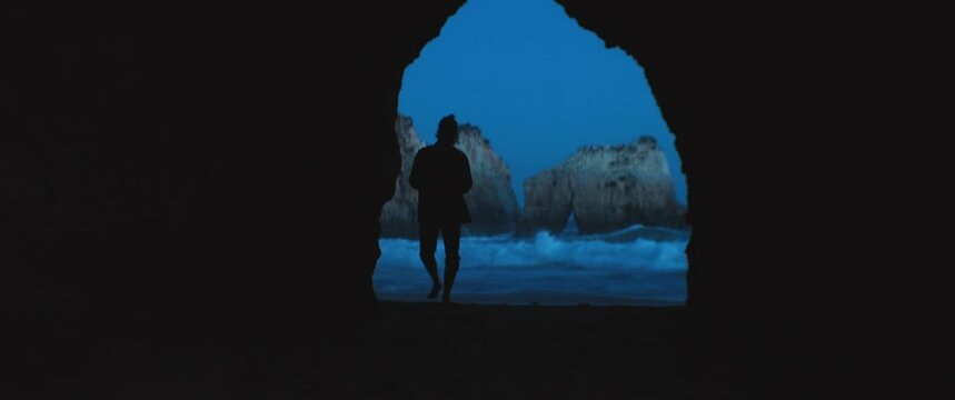 A man walking on the natural cave with the seaside landscape on the background