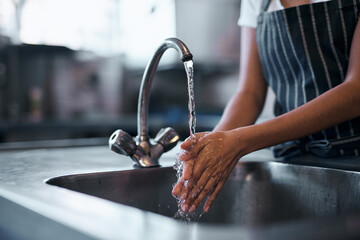 Good food starts with good hygiene. Cropped shot of a woman washing her hands in the sink of a commercial kitchen.