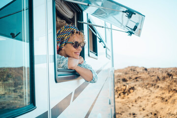 Happy young atractive woman admire and enjoy the view from modern camper van window. Alternative home and travel lifestyle people. Van life. Summer holiday vacation on vehicle. Free female smile - obrazy, fototapety, plakaty
