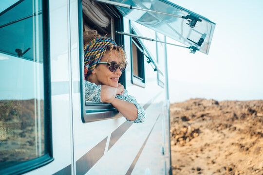 Happy young atractive woman admire and enjoy the view from modern camper van window. Alternative home and travel lifestyle people. Van life. Summer holiday vacation on vehicle. Free female smile