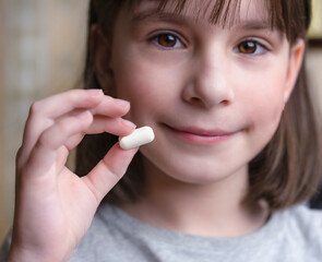 Een kind houdt een witte tablet vast. Medicijnen en synthetische vitamines. Het concept van drugsselectie. Behandeling voor kinderen.