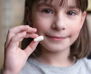 Poster Een kind houdt een witte tablet vast. Medicijnen en synthetische vitamines. Het concept van drugsselectie. Behandeling voor kinderen. © Albert Ziganshin
