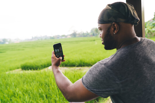 African American malein bandanna making selfie photo images while visiting rice fields at Vietnam using cellphone media app, millennial hipster guy shooting video vlog via smartphone