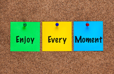 Three colored notes on a corkboard with words Enjoy Every Moment