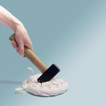 A Man Hand Holding Hammer Smashed  Sweet Meringue Pavlova Cake. Sky Blue Background.