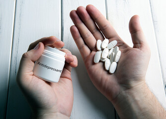 white pills and a jar with inscription antidepressant in human hand on a wooden table - obrazy, fototapety, plakaty