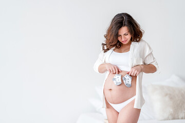 Cute pregnant woman holding socks for newborn