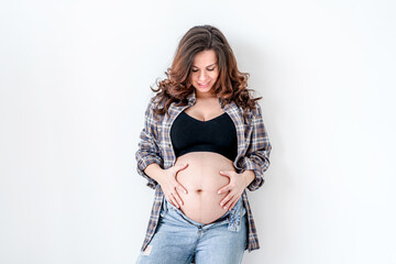 Beautiful young pregnant brunette woman in modern clothes with white background. The concept of motherhood and pregnancy