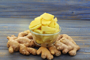 heap of peeled and cut Fresh ginger root spice in bowl with unpeeled ginger on wooden background 