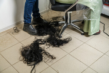 Cropped long female black hair on the floor next to the hairdresser's chair.