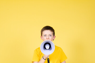 Angry boy speaking on megaphone looking straight to camera on yellow background with copy space.