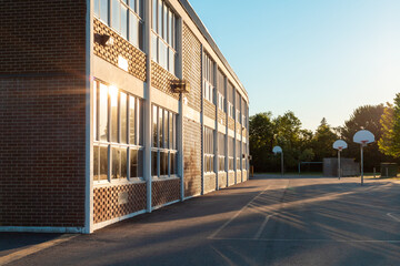 The exterior of the school building and school yard with a basketball court on a sunny evening. The...
