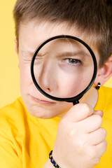 Closeup of cute boy looking at camera through loupe.