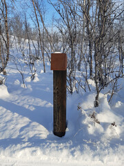 Naklejka premium Wooden post in Snowy lapland landscape. Hiking trail signage with snow on the polar circle under blue sky. Nature of the Nordic countries.