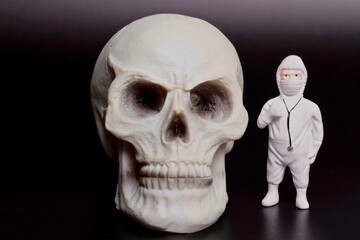 miniature figurine of a doctor with a protective suit and aa giant human skull on a black background
