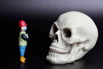 miniature figurine of a worker with a giant human skull on a black background