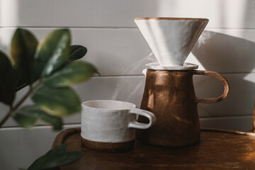 Morning coffee aesthetics. Modern ceramic cup, kettle and dripper for pour-over coffee in sunlight