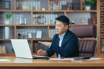 Fototapeta premium Asian businessman boss talking to colleagues on video call, looking at laptop screen, working in office, online meeting