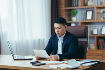 Accountant-auditor works in a classic office, calculates financial reports, Asian businessman works with computer and documents, paperwork