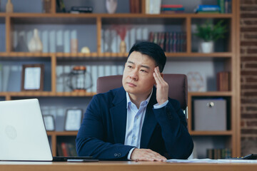 Asian businessman working in the office holding hands behind his head, tired has a severe headache, sick man at work