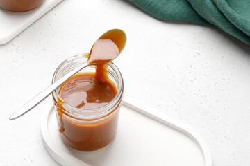 Liquid caramel on spoon on glass jar. Caramel drips from the spoon. Close up. Green napkin and white background