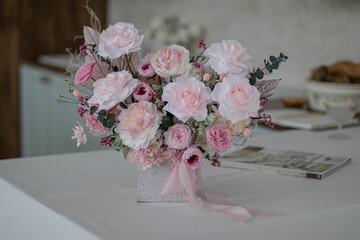 Beautiful bouquet of peonies and pink roses on the table. In the background is the interior of a modern white kitchen. Concept of home comfort.