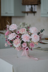 Beautiful bouquet of peonies and pink roses on the table. In the background is the interior of a modern white kitchen. Concept of home comfort.
