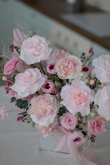 Beautiful bouquet of peonies and pink roses on the table. In the background is the interior of a modern white kitchen. Concept of home comfort.