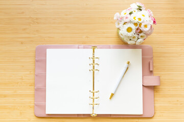 Flat lay, top view of a pastel pink diary flower bouquet and stationery on a wooden desk.
