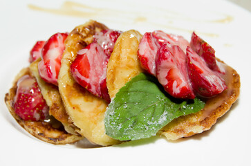 Fresh strawberries with baked pancakes and mint leaf in sugar sauce. Selective focus.