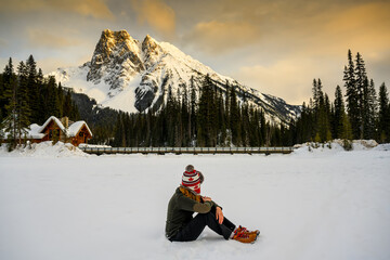 Casual woman sitting on the ice of the frozen Emerald Lake in the Yoho National Park, with Mount...
