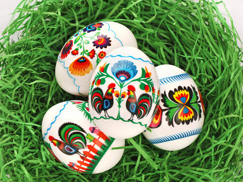 Four Colourful Easter Eggs with polish folk art motives thermal stickers in green paper grass nest. Polish traditional paper-cut with flowers and roosters from Lowicz region - wycinanka.