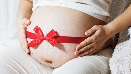 Pregnant woman belly with red ribbon. Family and maternity concept.