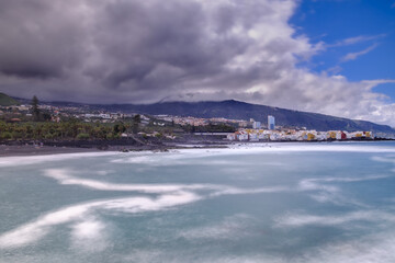 Naklejka na ściany i meble The Atlantic coast in the area of Playa Jardin in the background Punta Brava. The Atlantic Ocean on the coast of Puerto de la Cruz - the weather is changing - dramatic rain clouds are gathering.