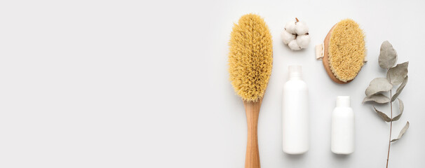 Wooden body massage brushes with natural bristles, white clean cosmetic bottles, eucalyptus branch, cotton flower on gray background. Organic accessories for health and beauty. Spa products. Flat lay