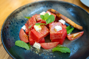 Summer salad with watermelon, tomatoes, feta cheese and basil on black plate in the wood table.