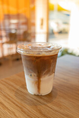 cold brewed iced latte coffee, showing separate in a layer the bottom as milk top by coffee shot in a plastic glass on wooden table in restaurant and cafe