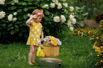 Little girl wipes her forehead after she finished washing clothes in nature.