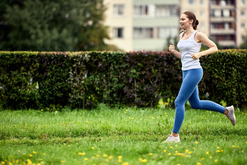 Jogging in city park in summer by young active woman.